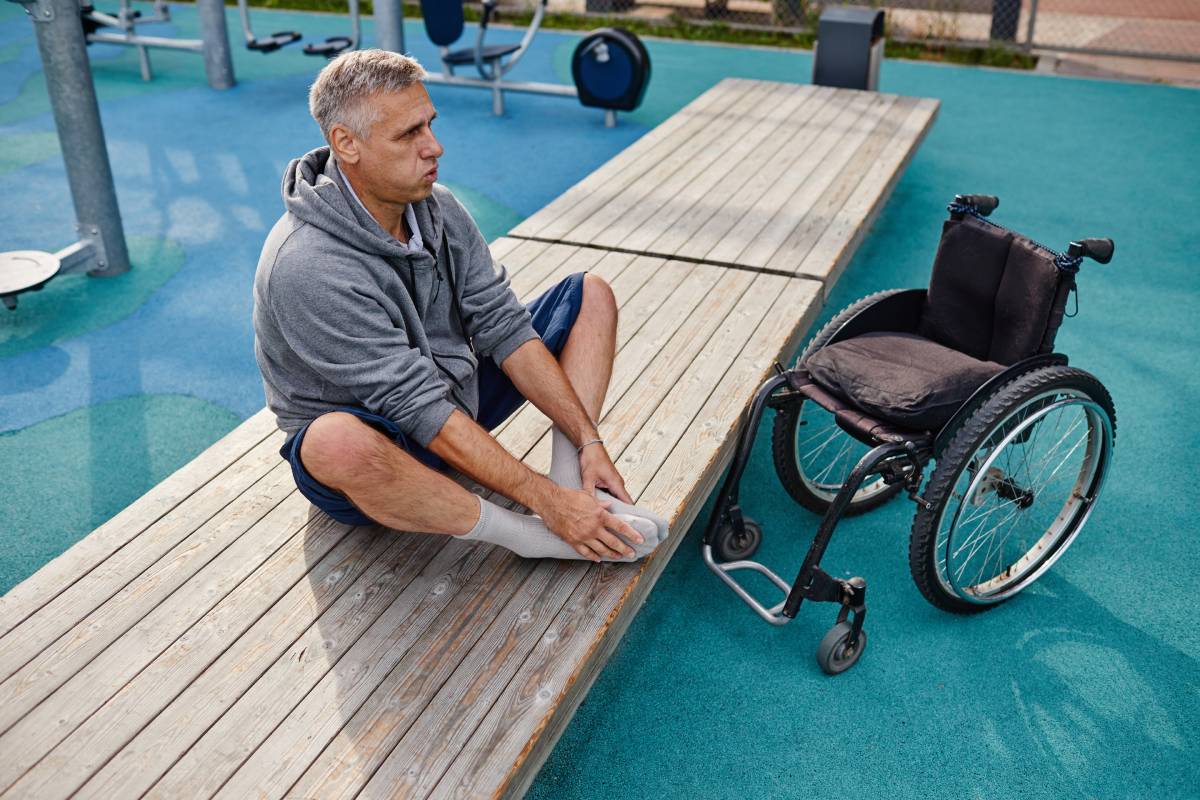 Mature man with disability sitting on the bench and doing breathing exercises while training outdoors