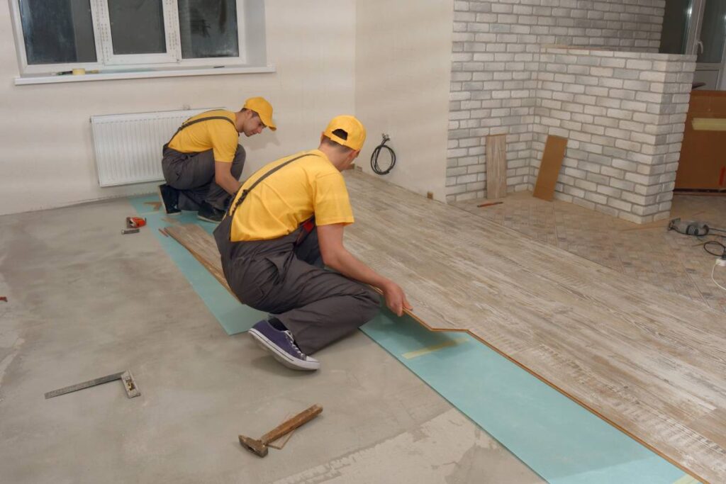 Team of builders make renovation of apartment. Construction workers laying floor board.