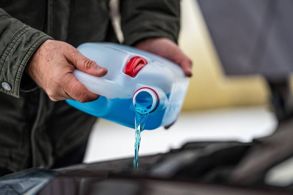 driver refilling the blue non-freezing windshield washer liquid in the tank of the car, closeup