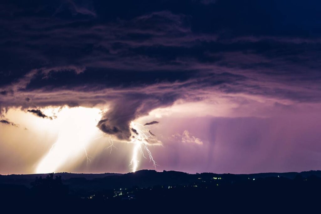 Night landscape on a background of thunderstorms. Rural silhouette and clouds with lightning flashes