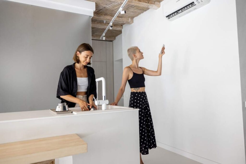 Stylish female couple cooking healthy vegan meals in white kitchen. Woman setting a temperature on the air conditioner