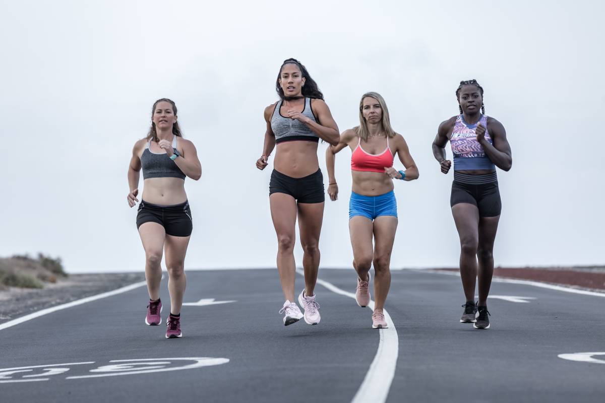 Full body multiethnic female friends in sportswear running on asphalt road towards camera during workout in outskirts