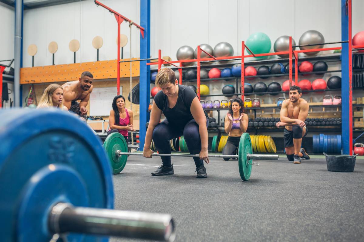 Concentrated woman ready to do weightlifting while her gym mates cheering her on