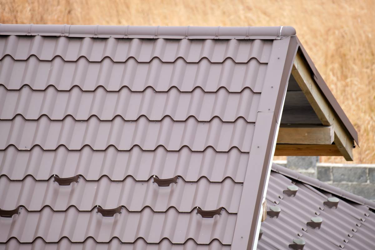Closeup snow guard for safety in winter on house roof top covered with steel shingles. Tiled covering of building.
