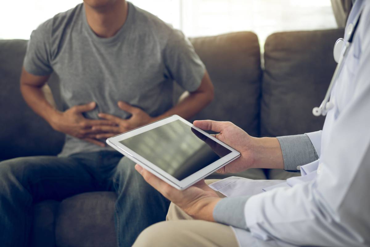 Doctor visited the patient while using tablet explaining about the patient stomach pain in the living room at home.