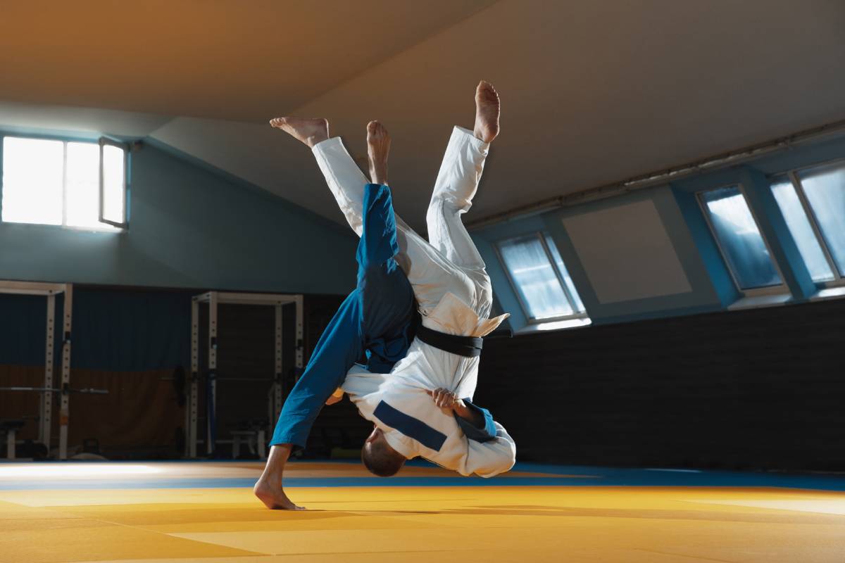 Two young judo caucasian fighters in white and blue kimono with black belts training martial arts in the gym with expression, in action, motion. Practicing fighting skills. Overcoming, reaching target.