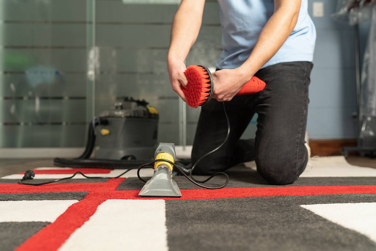 Laundry personnel cleaning carpet with special equipment. Young worker on his knees cleaning carpet.
